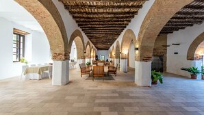 A spacious hall with a high ceiling, arched brick columns, and a central seating area with tables and chairs. - Los Pozos de  la Nieve Apartment Luna Rural Apartments, province of Sevilla (Constantina,)