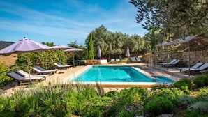 A rectangular pool with lounge chairs and umbrellas, surrounded by greenery and a stone wall. - Los Pozos de  la Nieve Apartment Luna Rural Apartments, province of Sevilla (Constantina,)