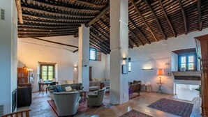 A spacious living area with a high ceiling, exposed wooden beams, and a mix of seating arrangements including sofas and chairs.