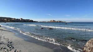 En kustnära strand med vågor, en fyr och byggnader i bakgrunden.