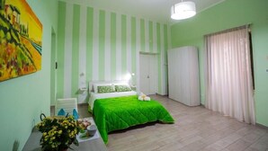 Un dormitorio con una cama, una mesita de noche, una silla, un cuadro y una ventana con cortinas.