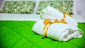 Una cama bien hecha con toallas blancas y una cinta dorada, sobre un edredón verde.