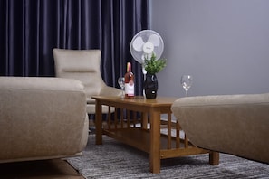 A living room with a wooden coffee table, a bottle of wine, a glass, and a fan. - The Candela Hotel (Siaya)