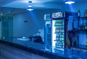 A bar area with a refrigerator stocked with beverages, a counter, and a seating area. - The Candela Hotel (Siaya)