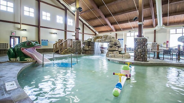 An indoor pool with a frog sculpture, a water slide, and a small watercraft.