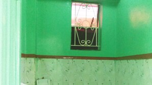 A small bathroom with a toilet, a window with decorative bars, and a wall with a floral pattern.