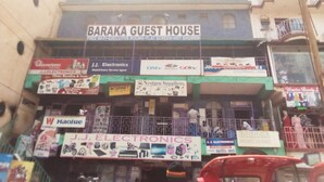 A multi-story building with a sign for 'Baraka Guest House' advertising executive rooms, a flat-screen TV, and a hot shower.