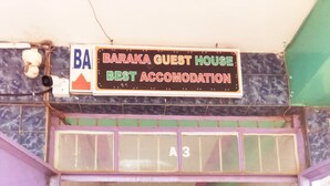 A hotel entrance with a reception desk, a sign above stating "Baraka Guest House Best Accommodation," and a tiled floor.