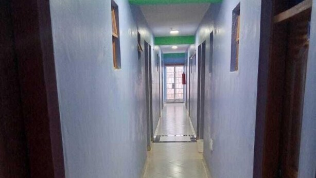 A long, narrow hallway with blue walls and a tiled floor, leading to a door at the end. - Beston Hotel Bungoma (Chwele)