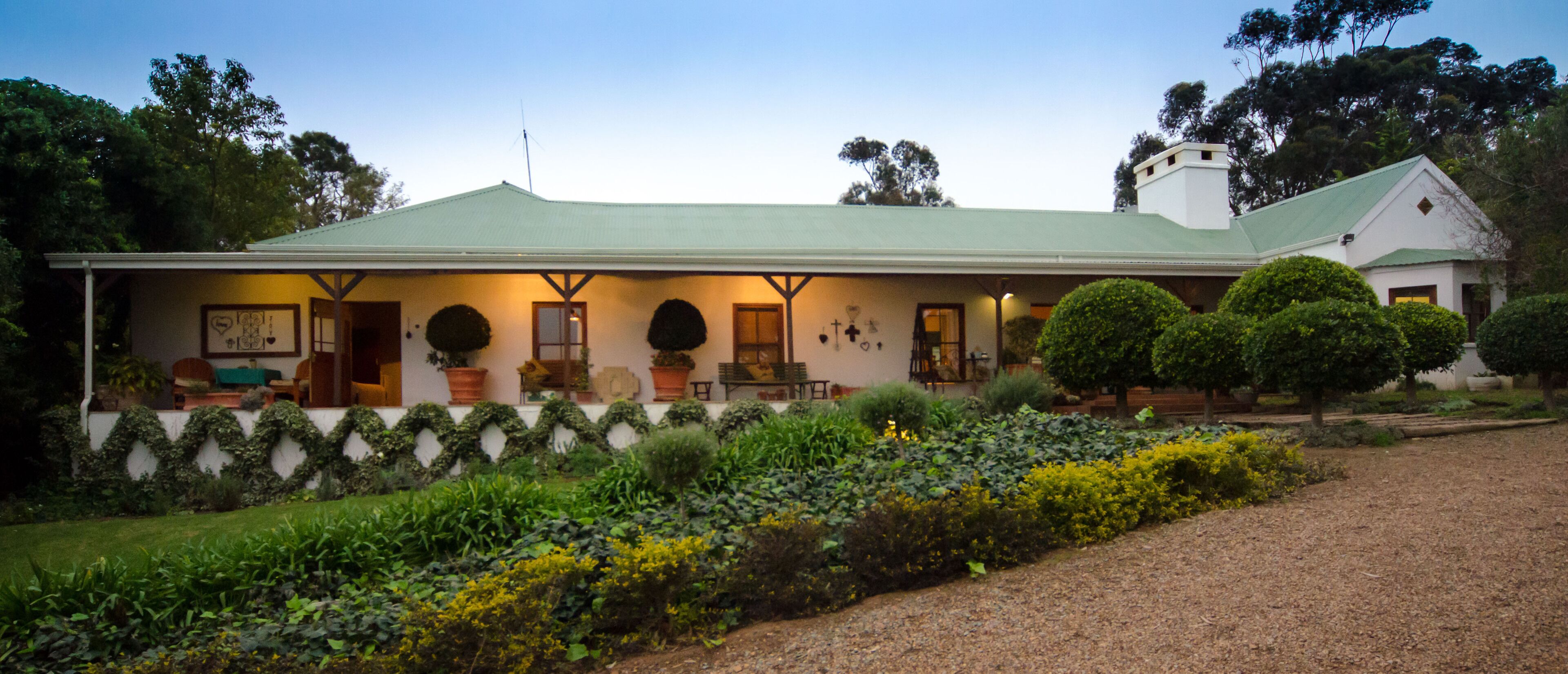 A house with a green roof, a porch with potted plants, and a garden with various shrubs and flowers.