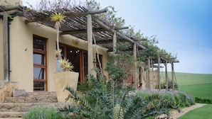 A house with a stone facade, wooden pergola, and a well-maintained garden with various plants and a stone pathway.