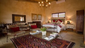 A cozy room with a bed, two chairs, a coffee table, and a chandelier.