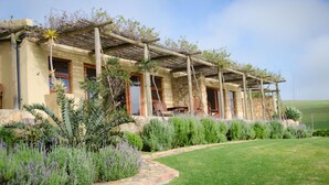 A two-story house with a pergola over the patio area, surrounded by a well-maintained garden with various shrubs and a lawn.