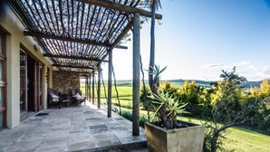 A covered patio with stone flooring, outdoor seating, and a view of a green landscape.
