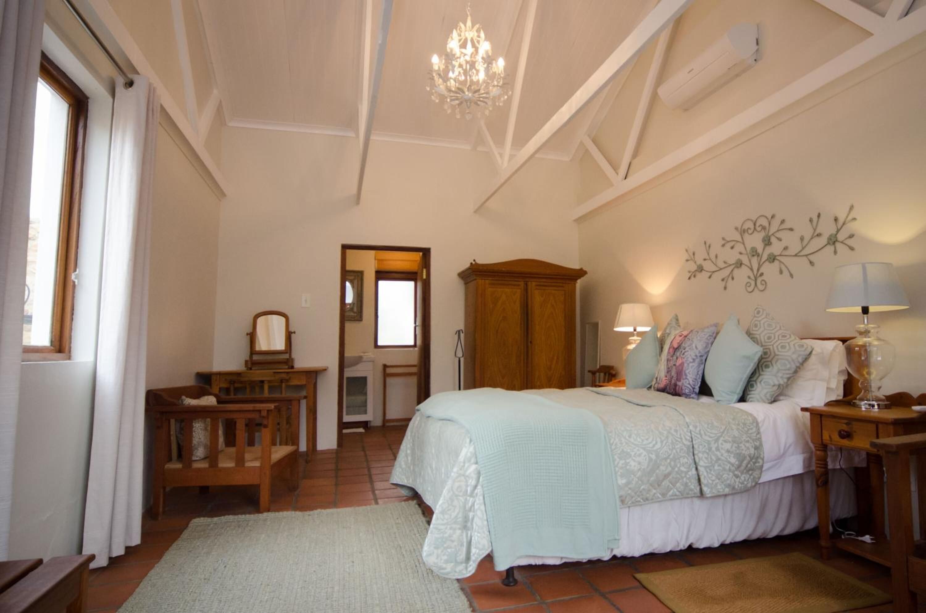 A bedroom with a large bed, a wooden wardrobe, a chandelier, and a wall-mounted lamp.