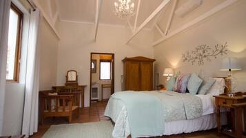 A bedroom with a large bed, a wooden wardrobe, a chandelier, and a wall-mounted lamp.
