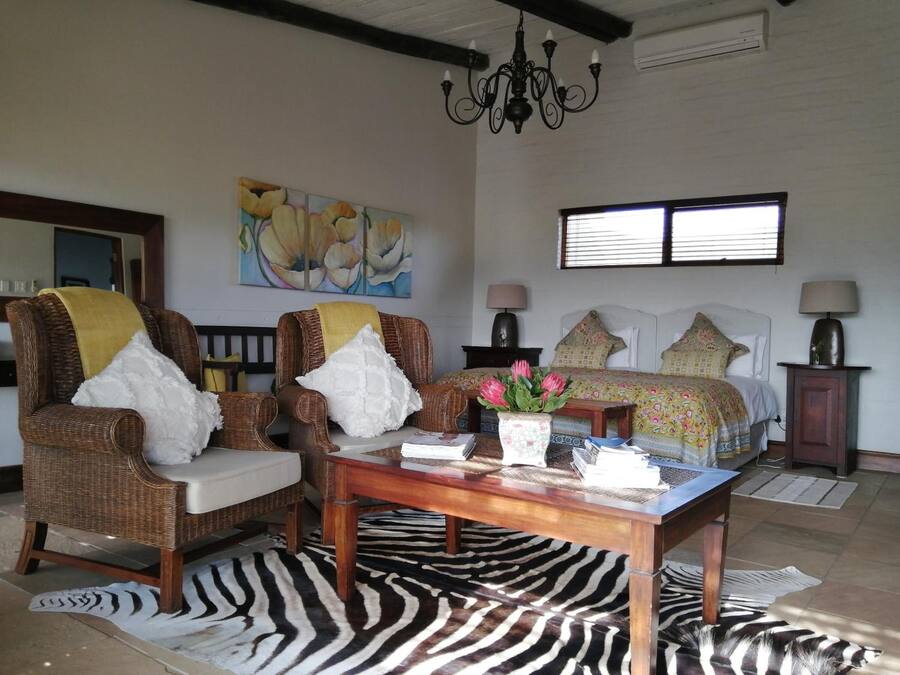 Una habitación amplia con una cama grande, dos sillones de mimbre, un tapete estampado con diseño de cebra y un cuadro de flores en la pared.