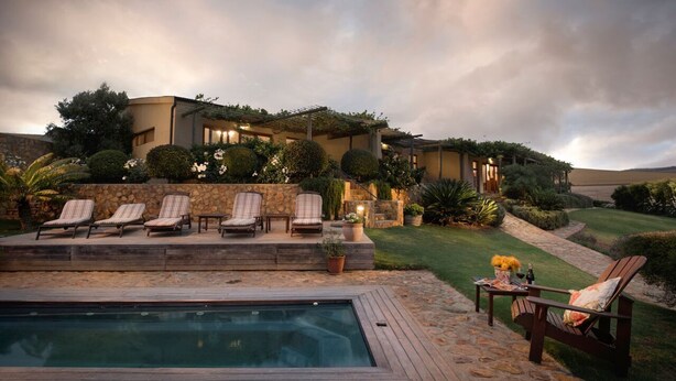 A poolside area with lounge chairs, a hot tub, and a stone wall.