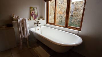 A bathroom with a freestanding bathtub, a window with a stone wall view, and a painting on the wall.