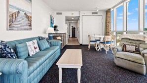 Una habitación con sofá, una mesa de centro, una mesa de comedor con sillas y vistas amplias a través de grandes ventanales.