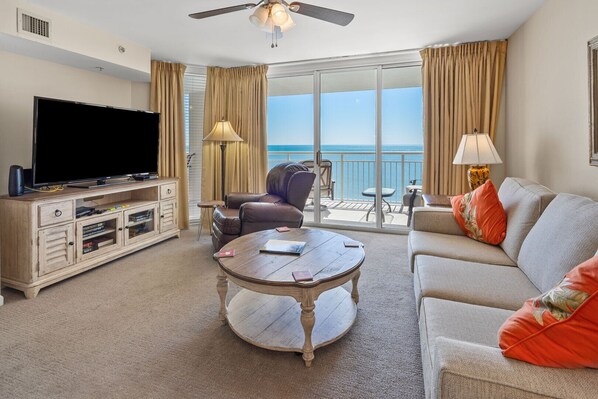 Une chambre d’hôtel équipée d’un téléviseur à écran plat, d’un meuble de rangement en bois, d’un canapé en cuir, d’une table basse ronde et d’un balcon avec vue sur la mer.