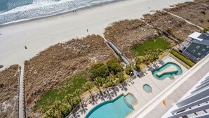 An aerial view of a beachfront property with a swimming pool, a beach, and a staircase leading to a building.