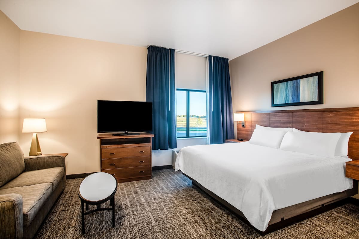 Una habitación de hotel con cama, televisor, sofá, una mesita y ventana con cortinas.