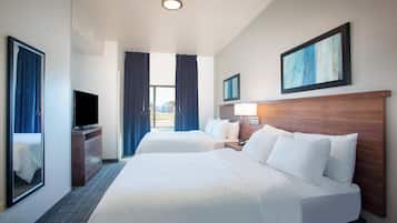 Habitación de hotel con dos camas, televisión, escritorio y ventana con cortinas.