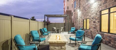 An outdoor patio with a fire pit, seating, and a view of a building.