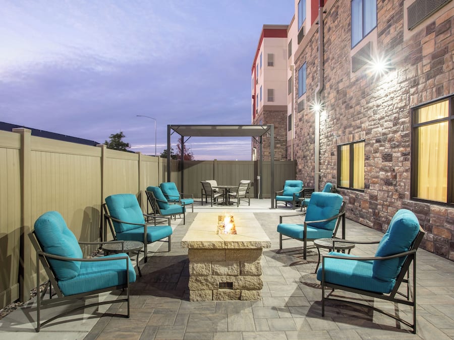 An outdoor patio with a fire pit, seating, and a view of a building.