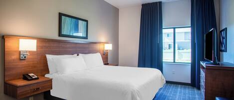 Habitación de hotel con cama, lámparas de noche, teléfono, televisión y ventana con cortinas.