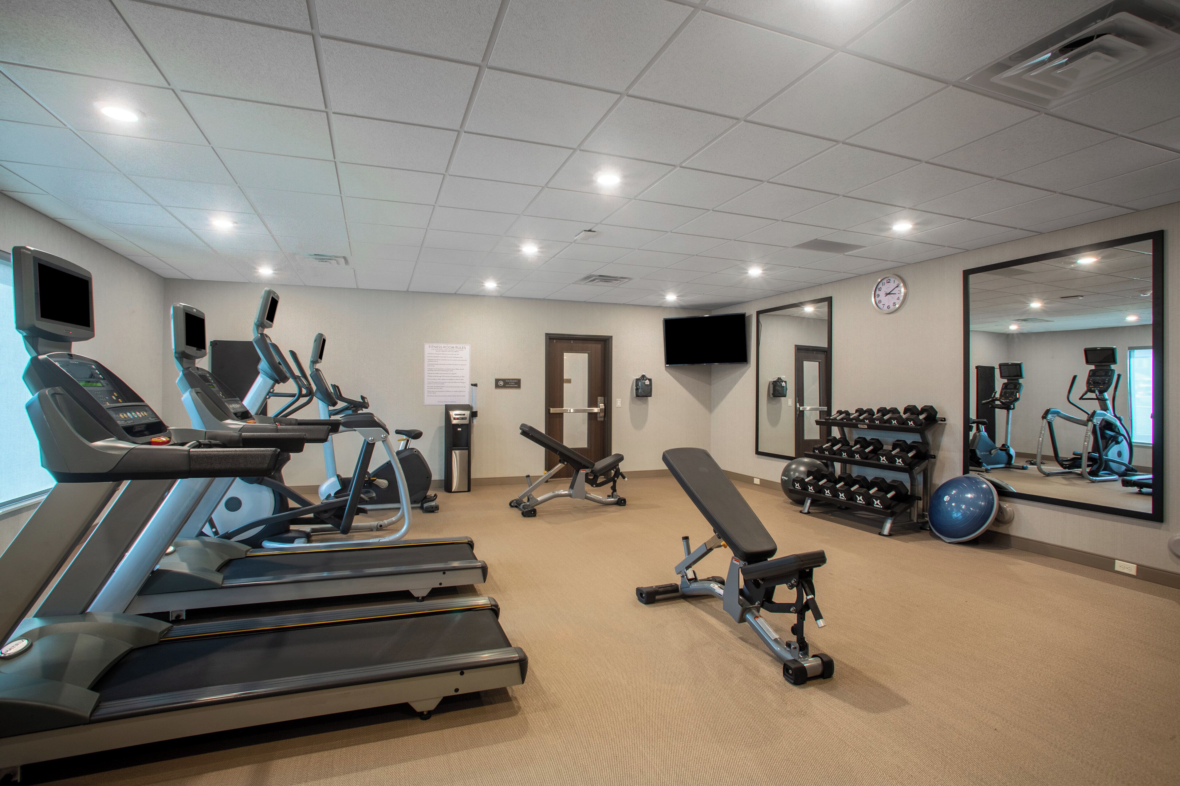 A gym with treadmills, elliptical machines, a bench press, dumbbells, and a large mirror.