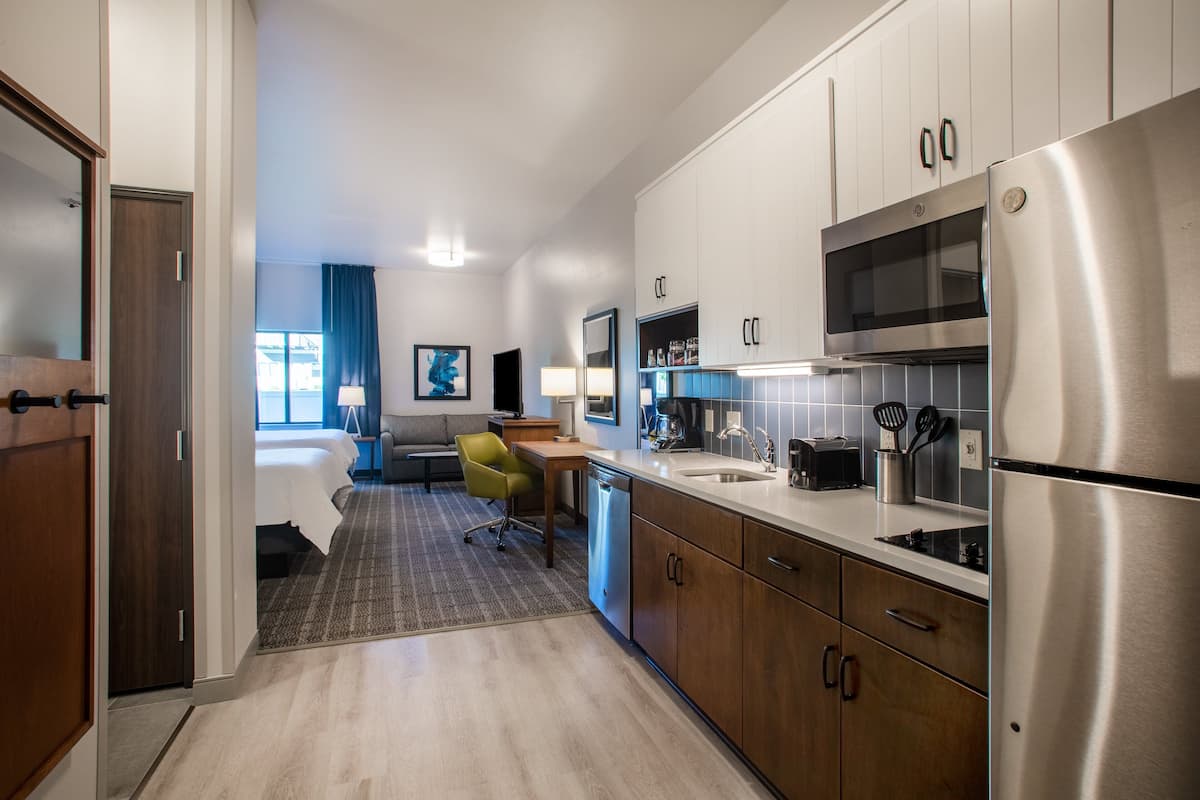 Una habitación de hotel moderna con kitchenette, una cama, un escritorio y una silla.