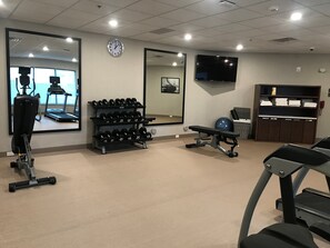 A gym with exercise equipment, a mirror, a clock, and a television.