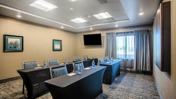 A conference room with a long table, chairs, water bottles, a flat-screen TV, and a window with curtains.