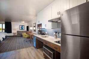 Een moderne hotelkamer met kitchenette, bed, zithoek en uitzicht op het omliggende landschap.