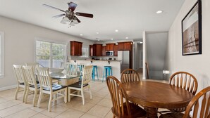 A modern kitchen with wooden cabinets, a central island, and a dining area with a round table and chairs. - Charmed home w/private pool, game room, wet bar, covered porches, sun deck, walk to beach (North Myrtle Beach)
