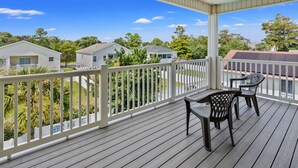 A covered outdoor deck with a table and chairs, surrounded by a white railing, overlooking a residential area with houses and trees. - Charmed home w/private pool, game room, wet bar, covered porches, sun deck, walk to beach (North Myrtle Beach)