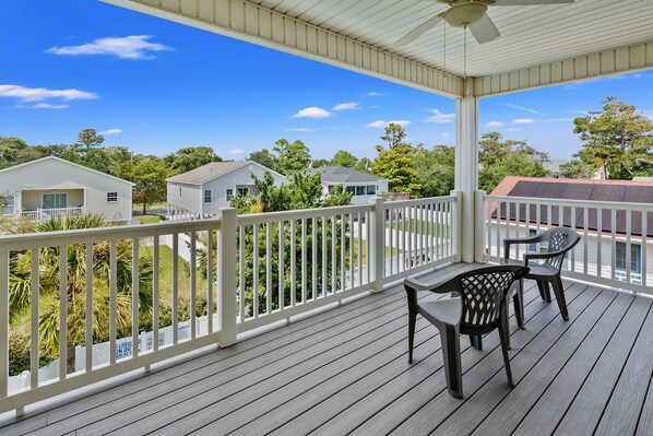 A covered outdoor deck with a table and chairs, surrounded by a white railing, overlooking a residential area with houses and trees. - Charmed home w/private pool, game room, wet bar, covered porches, sun deck, walk to beach (North Myrtle Beach)
