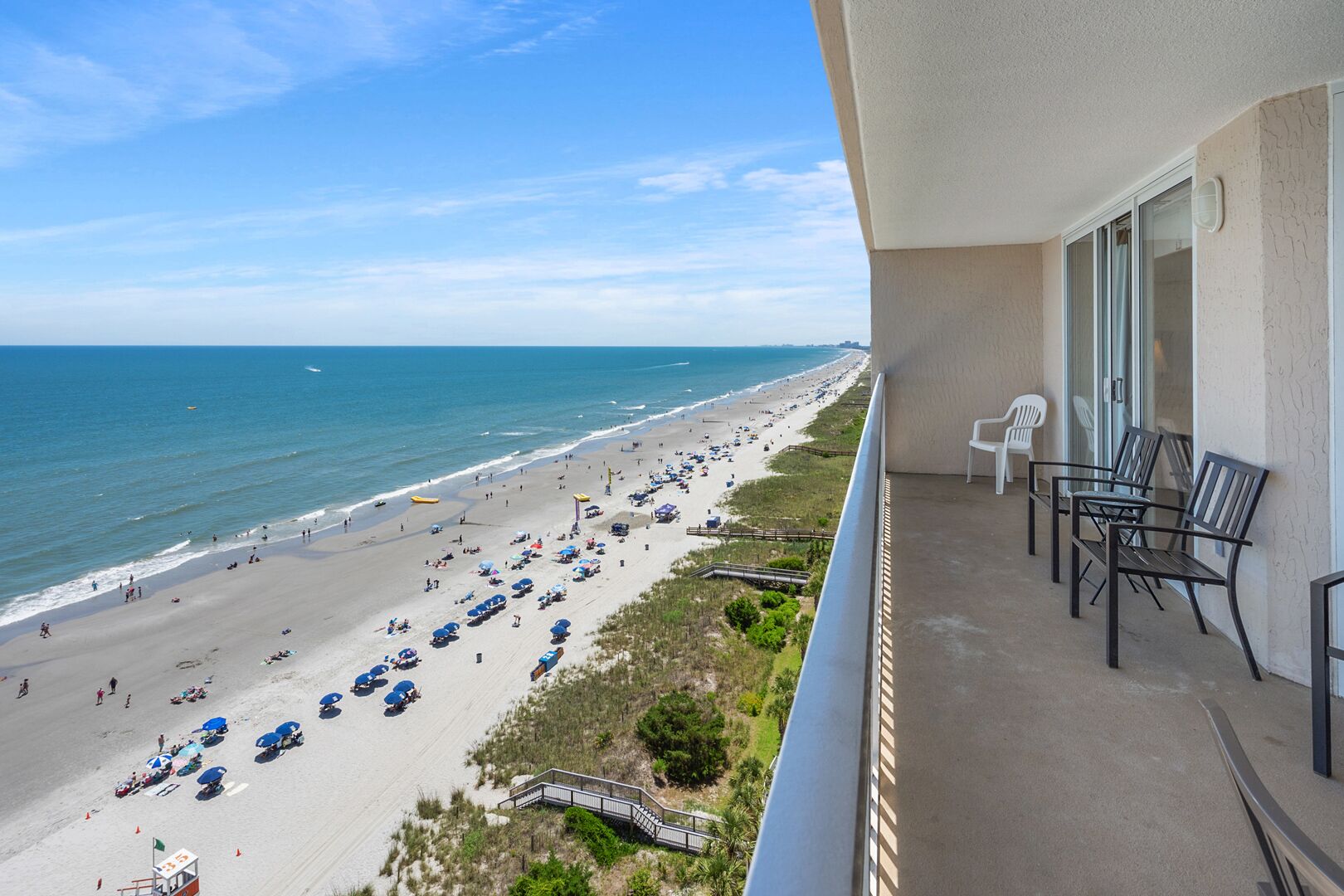 A balcony with a view of a beach, outdoor seating, and a lifeguard tower.