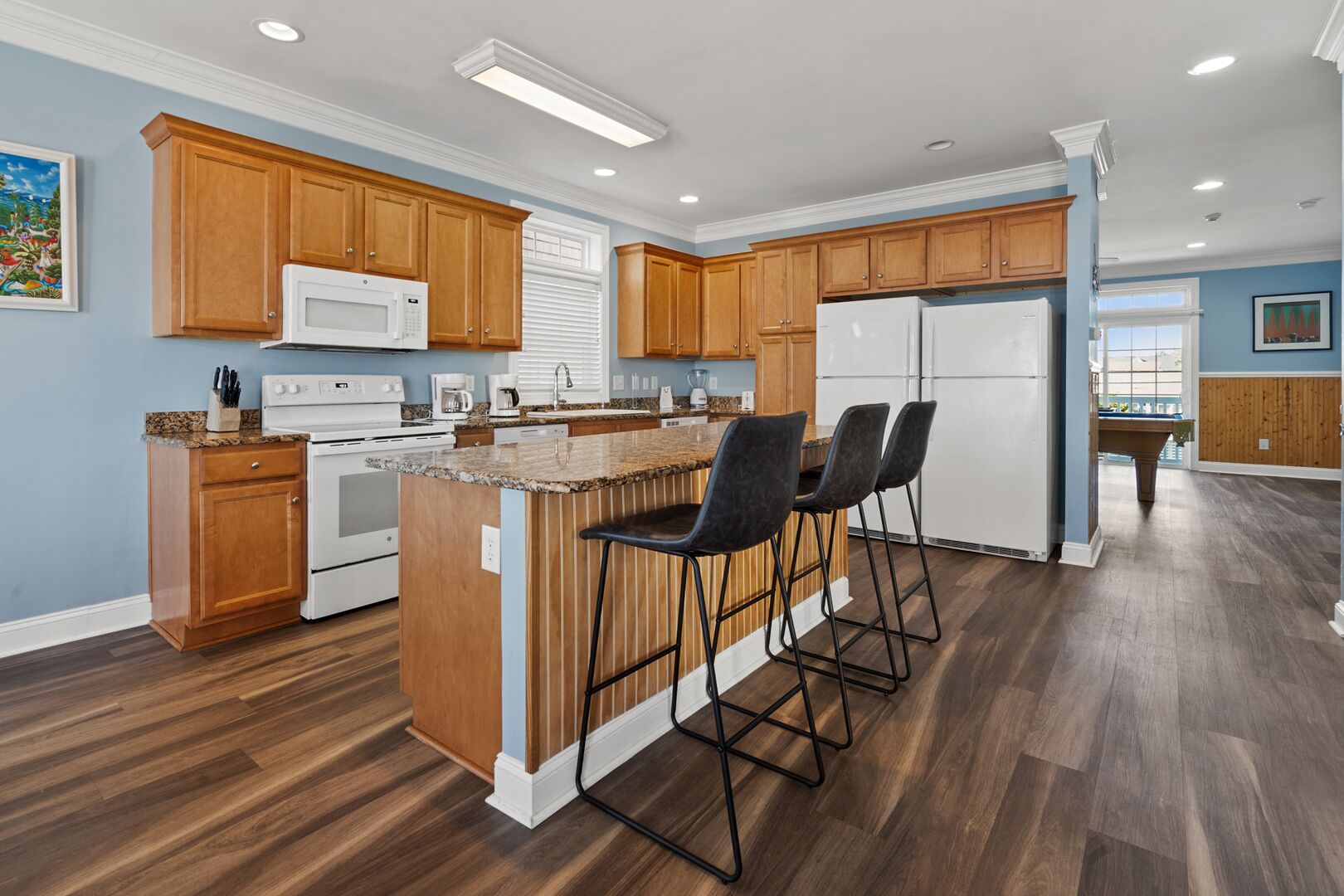 Een moderne keuken met houten kastjes, een centraal eiland met barstoelen, en een koelkast.