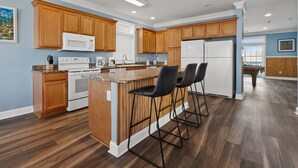 A modern kitchen with wooden cabinets, a central island with bar stools, and a refrigerator.