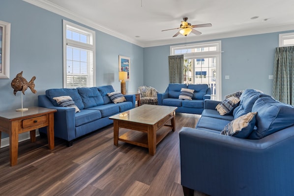 Ein Wohnzimmer mit blauen Sofas, einem Holztisch und einem Deckenventilator.