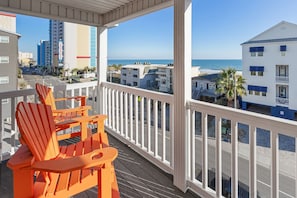 Ein Balkon mit orangefarbenen Adirondack-Stühlen, einem weißen Geländer und Blick auf Strand und Meer.