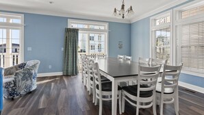 A dining room with a large table and white chairs, blue walls, and a patterned armchair.