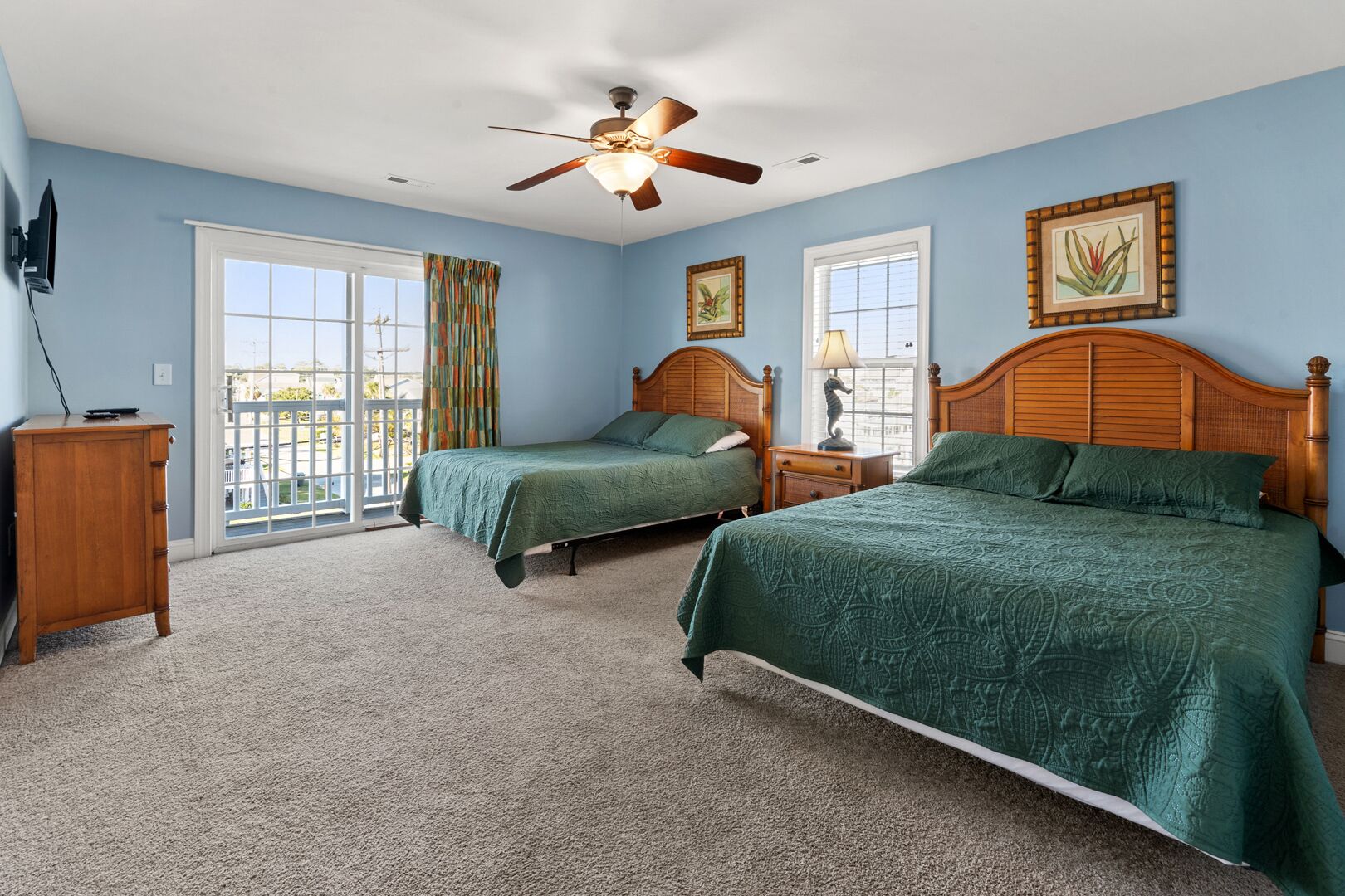 A bedroom with two beds, a ceiling fan, and a large window.