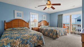 A bedroom with two beds, a ceiling fan, and a view of the ocean through large windows.