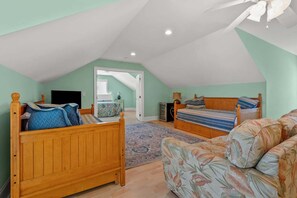 Ein Schlafzimmer mit schrägem Dach, zwei Betten, einem Sofa, einem Fernseher und einer Tür zu einem anderen Raum.