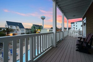 A wooden deck with a railing, overlooking a beach with houses and a clear sky.