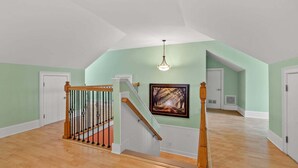 Ein großzügiger Innenraum mit einer Holztreppe, einem Deckenventilator und einem gerahmten Bild an der Wand.